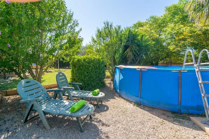 A garden seating area beside a blue above-ground pool, surrounded by greenery.