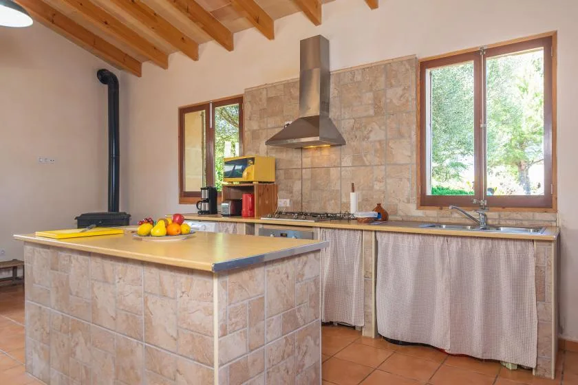 Una cocina rústica con una isla revestida de azulejos, una cocina y grandes ventanas.
