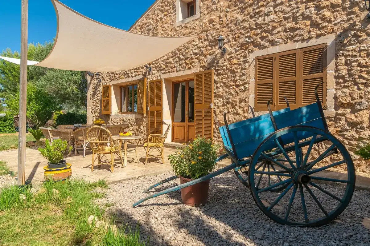 Patio de una casa de piedra con asientos al aire libre y un carro azul en primer plano.