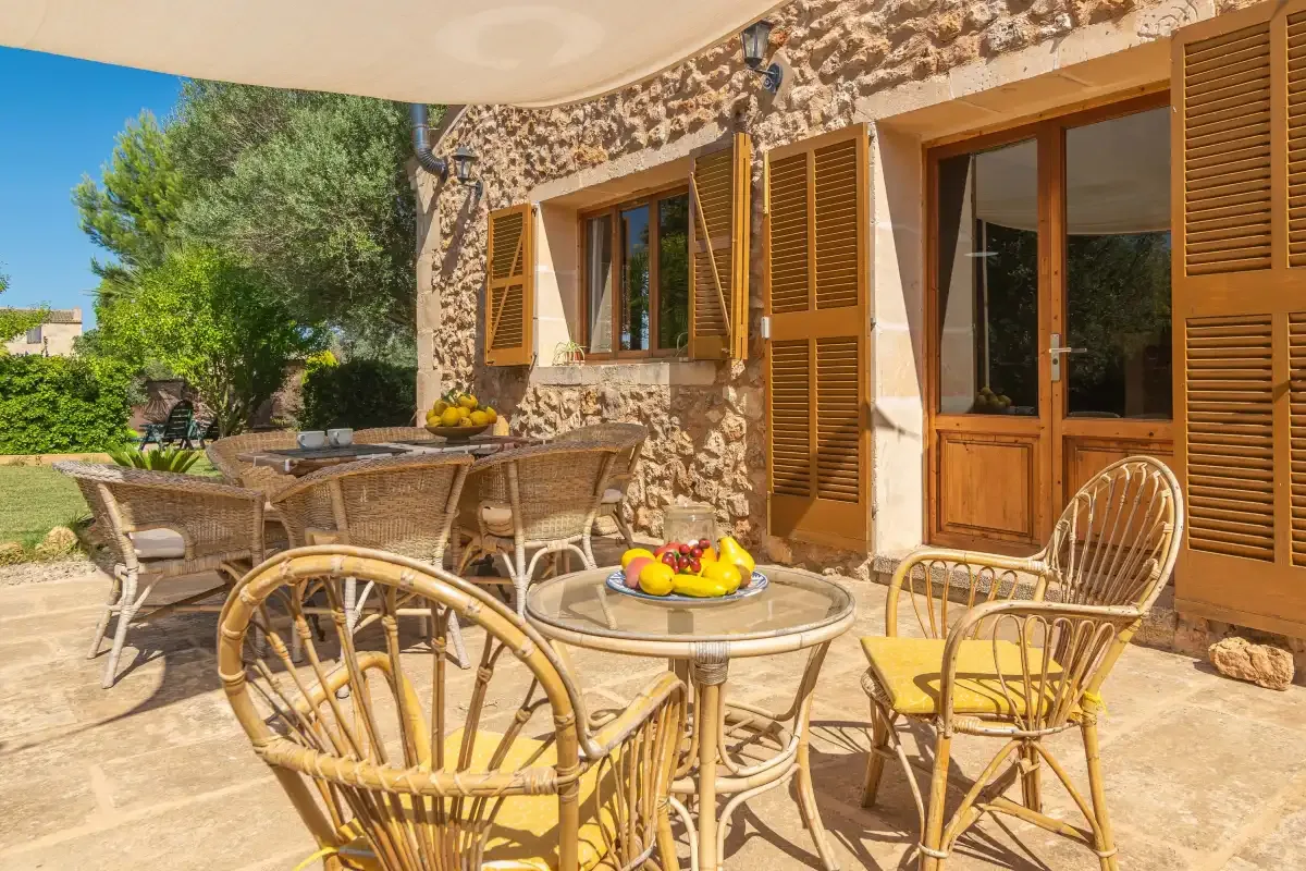 Un patio de una casa de piedra tiene asientos de mimbre y mesas bajo un toldo.