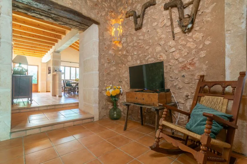 Una sala de estar rústica con televisor, pared de piedra y asientos de madera.