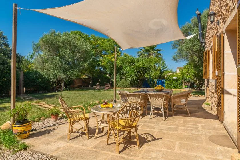 A shaded outdoor patio has a dining table and seating overlooking a leafy garden.