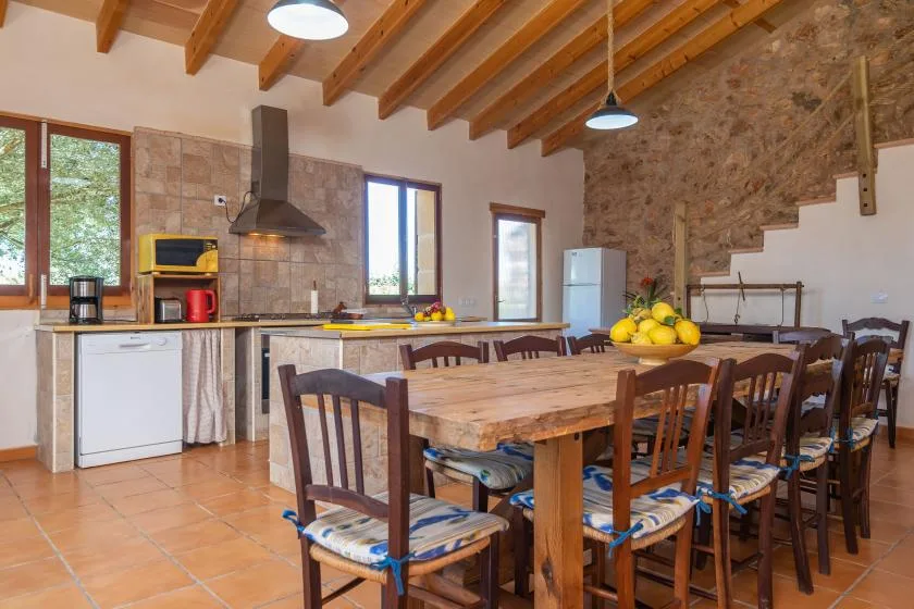 Un comedor con una larga mesa de madera y sillas junto a una cocina.