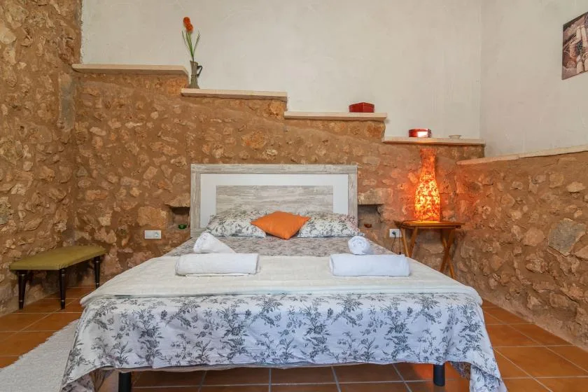 Dormitorio con una cama doble, ropa de cama estampada y paredes de piedra.