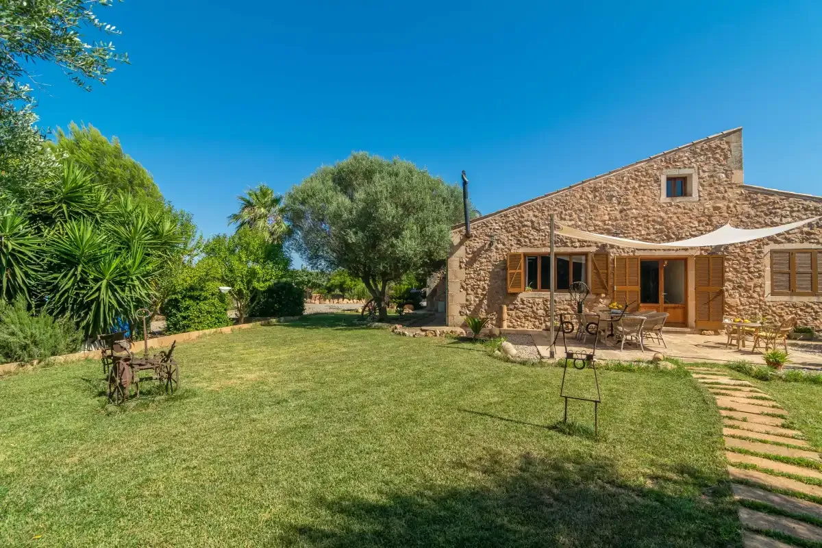 Una casa de piedra da a un jardín con césped, árboles y asientos al aire libre.
