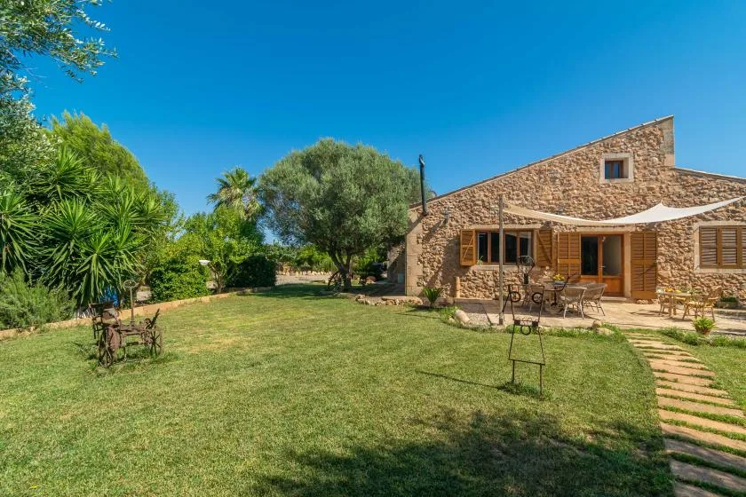 Una casa de piedra da a un jardín con césped, árboles y asientos al aire libre.
