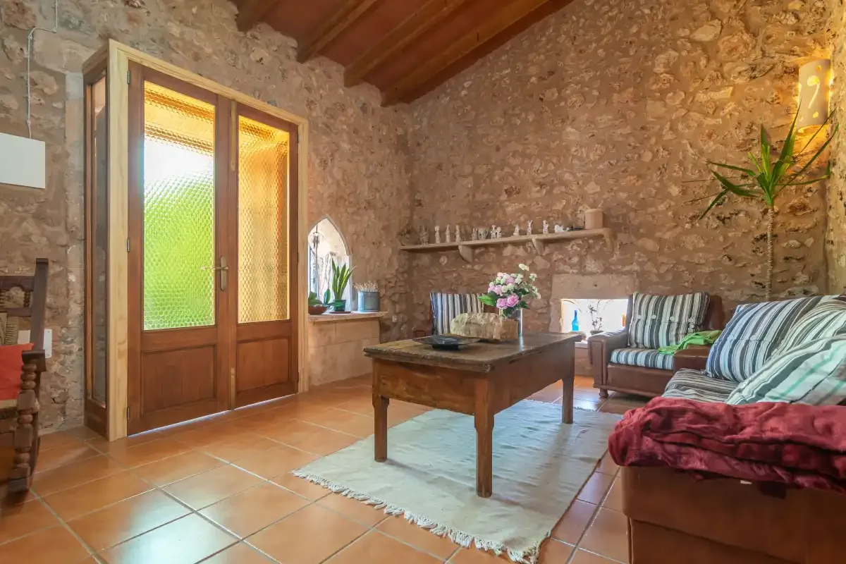 Una sala de estar rústica con paredes de piedra, vigas de madera y asientos alrededor de una mesa de centro.