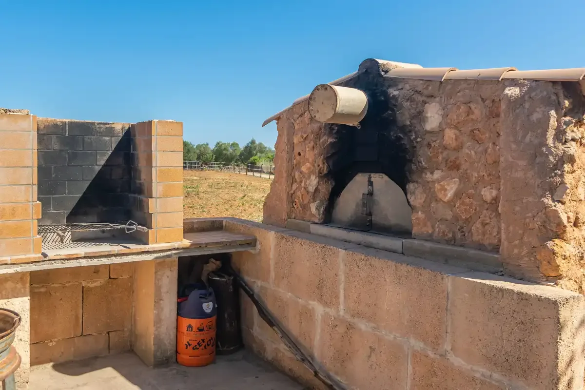 Un horno de piedra exterior y una encimera de obra están junto a una pequeña zona de cocina alicatada.
