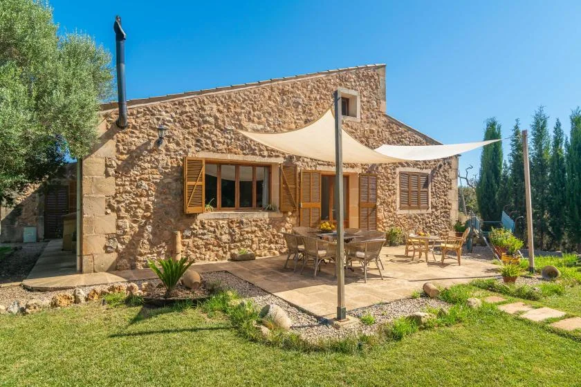 Una casa de piedra con un patio exterior sombreado y asientos junto al césped.