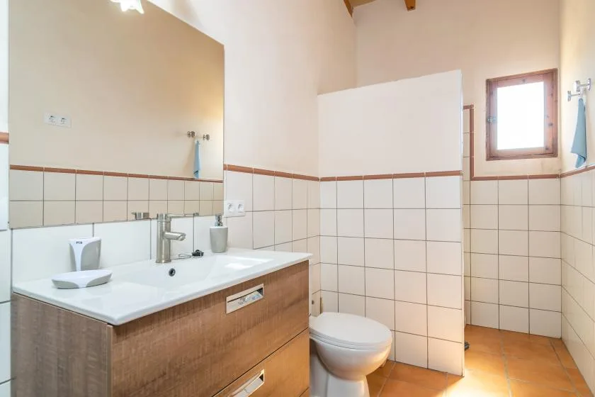 Un baño alicatado con lavabo, inodoro y una ventana pequeña.