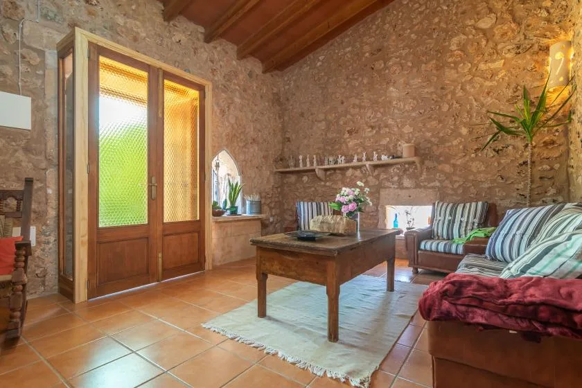 Una sala rústica con asientos de madera, una mesa de centro y paredes de piedra.