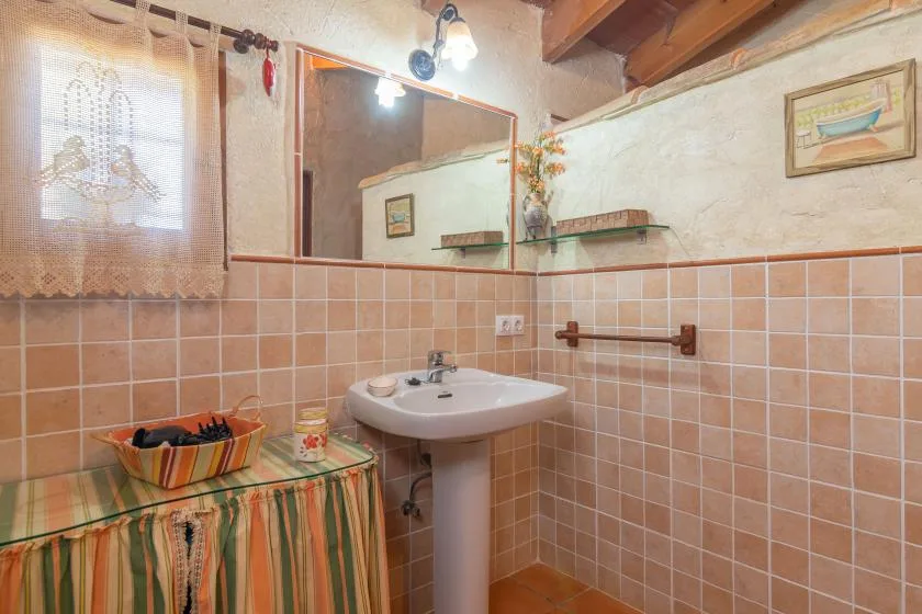 Un baño alicatado con lavabo, espejo y una ventana pequeña.