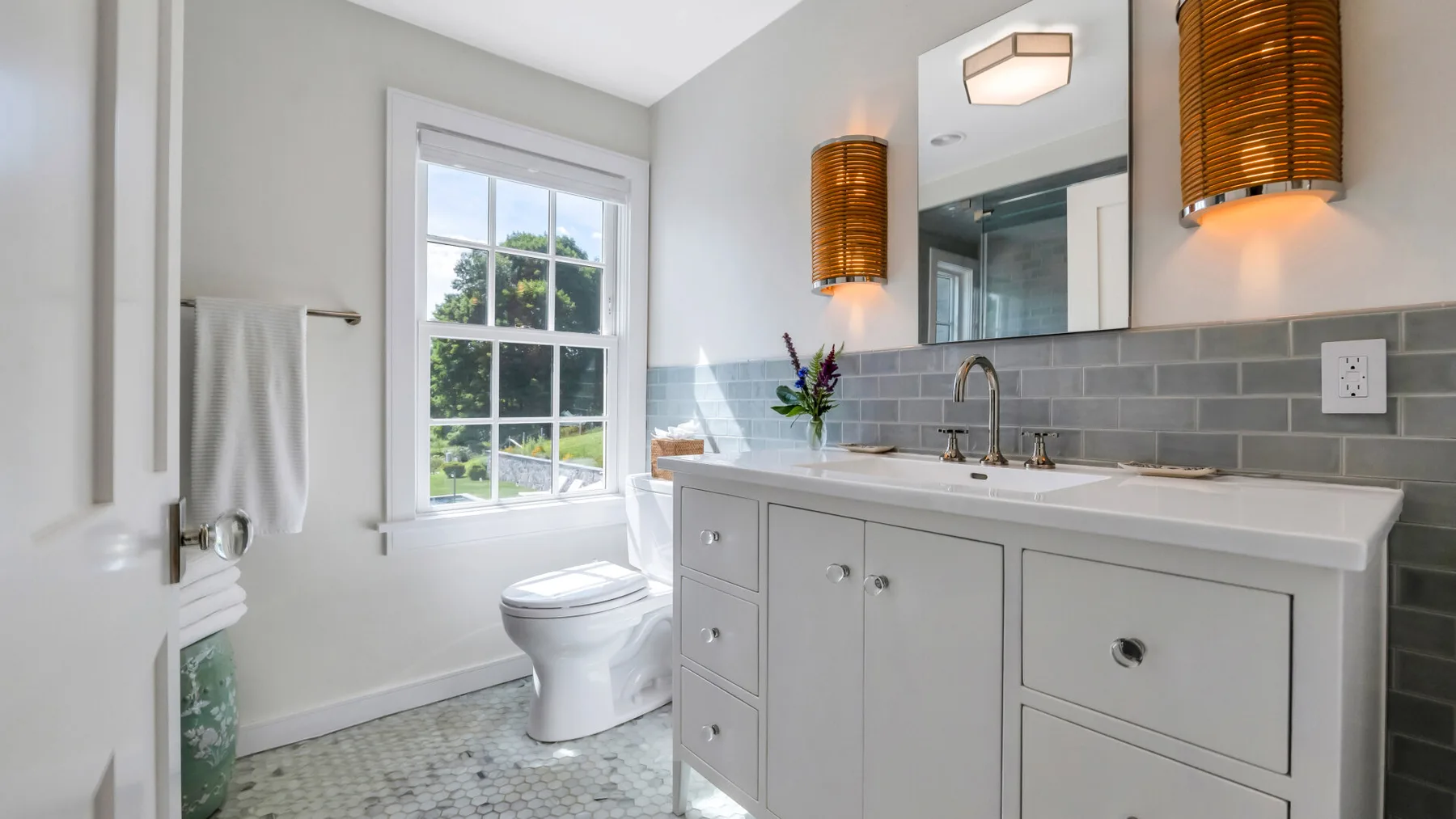 A bright bathroom with a long vanity, tiled backsplash, and window.