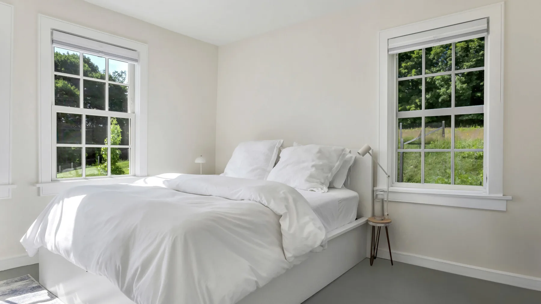 A bright bedroom with a white bed between two large windows.