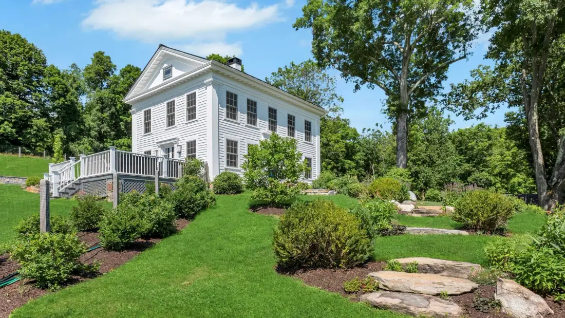 A white house stands beside a landscaped lawn and garden.