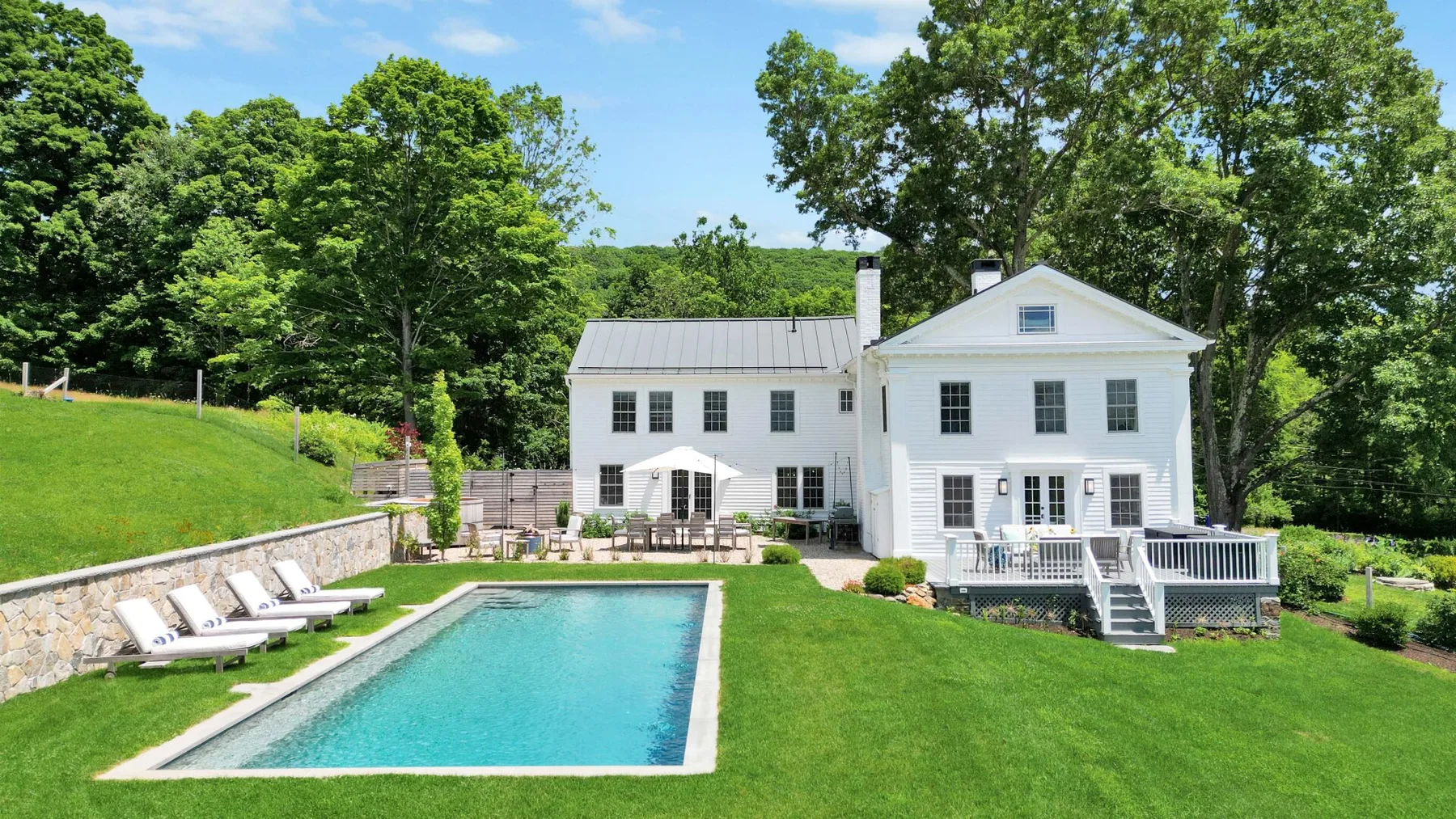 A white house stands behind a swimming pool and broad green lawn.