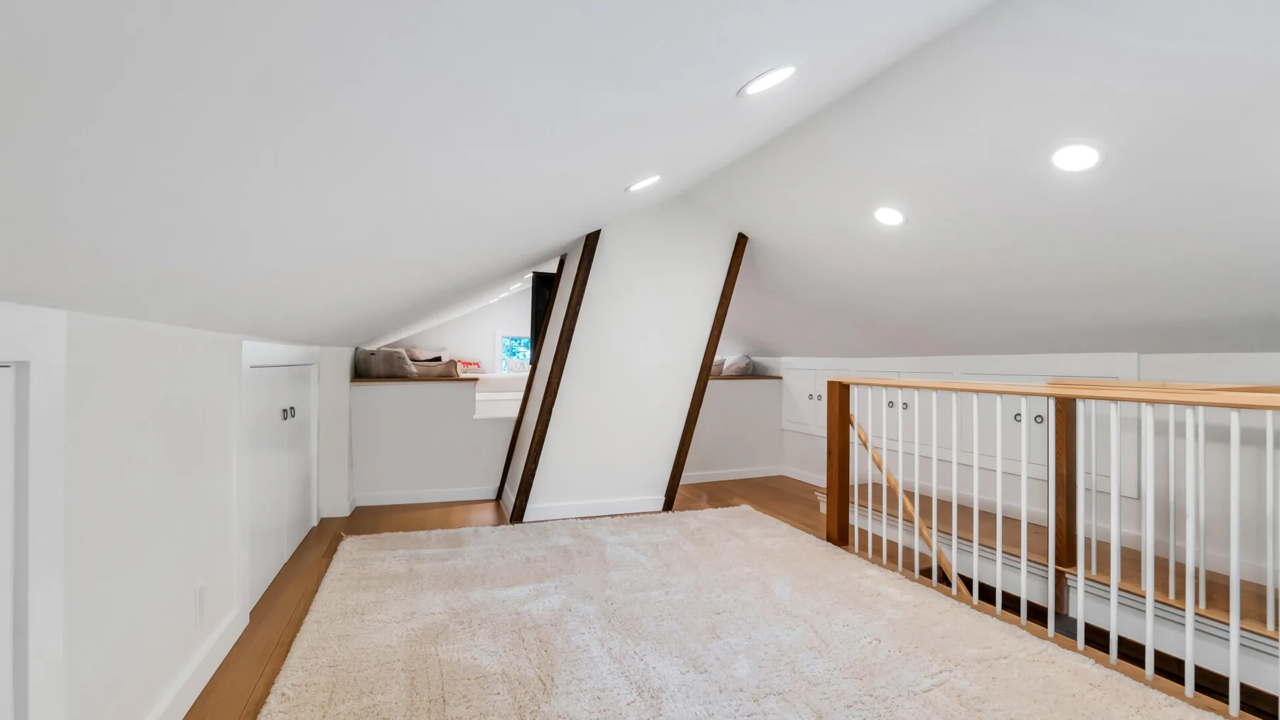A carpeted loft area sits beneath a sloped ceiling beside a railing.