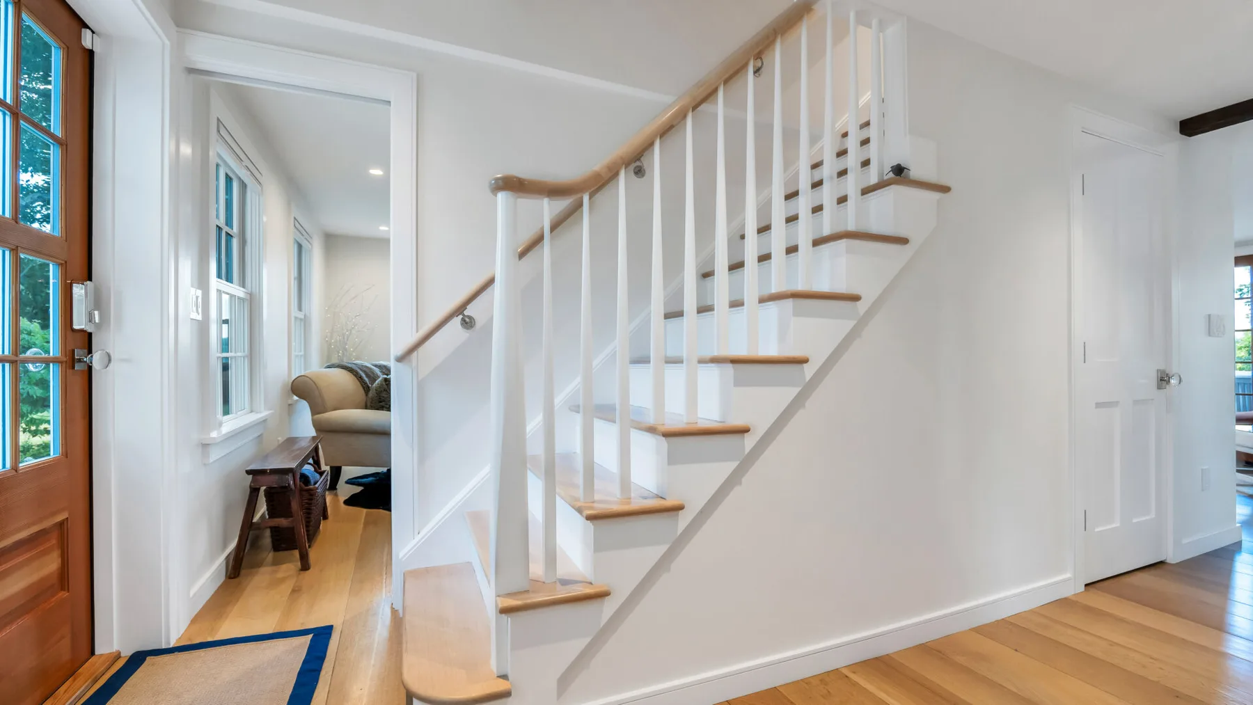 A bright interior hallway features a wooden staircase and light wood flooring.