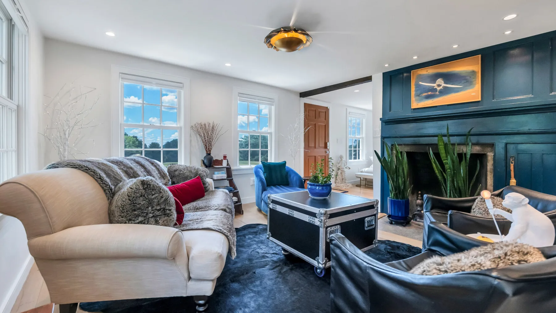 A bright living room with seating, large windows, and a dark fireplace wall.