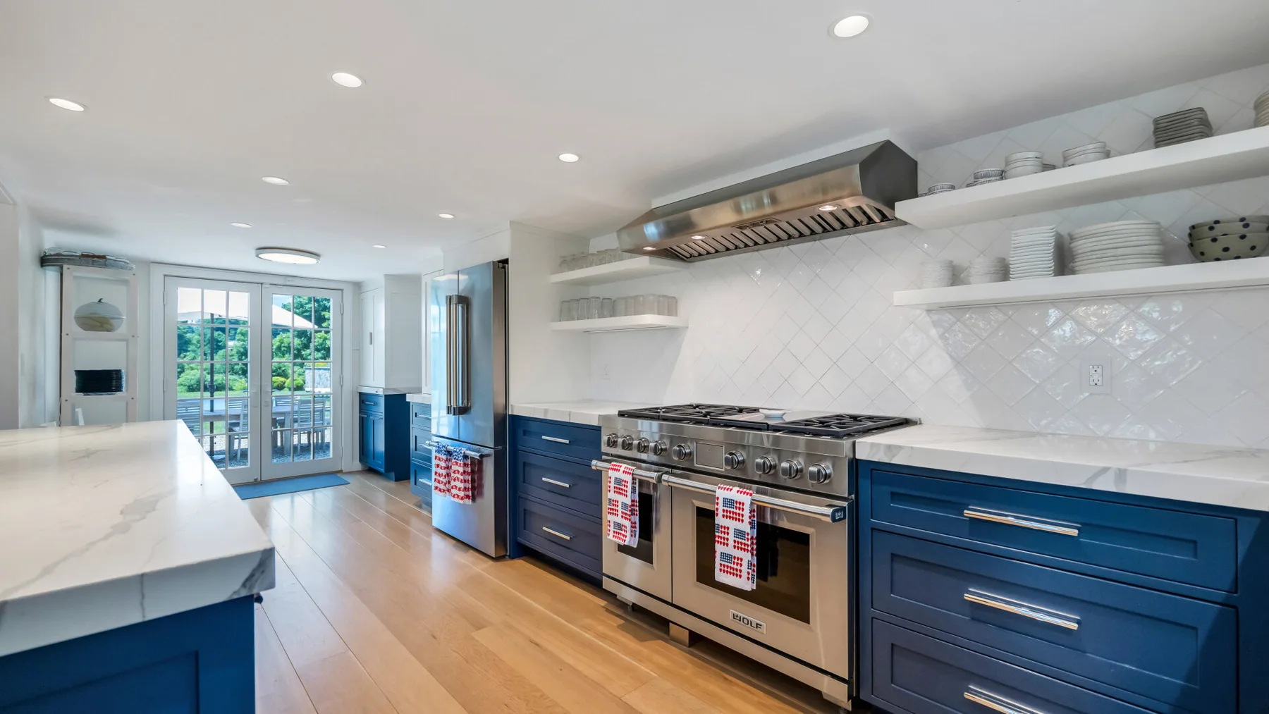 A bright kitchen with blue cabinets, stainless steel appliances, and a long white countertop.