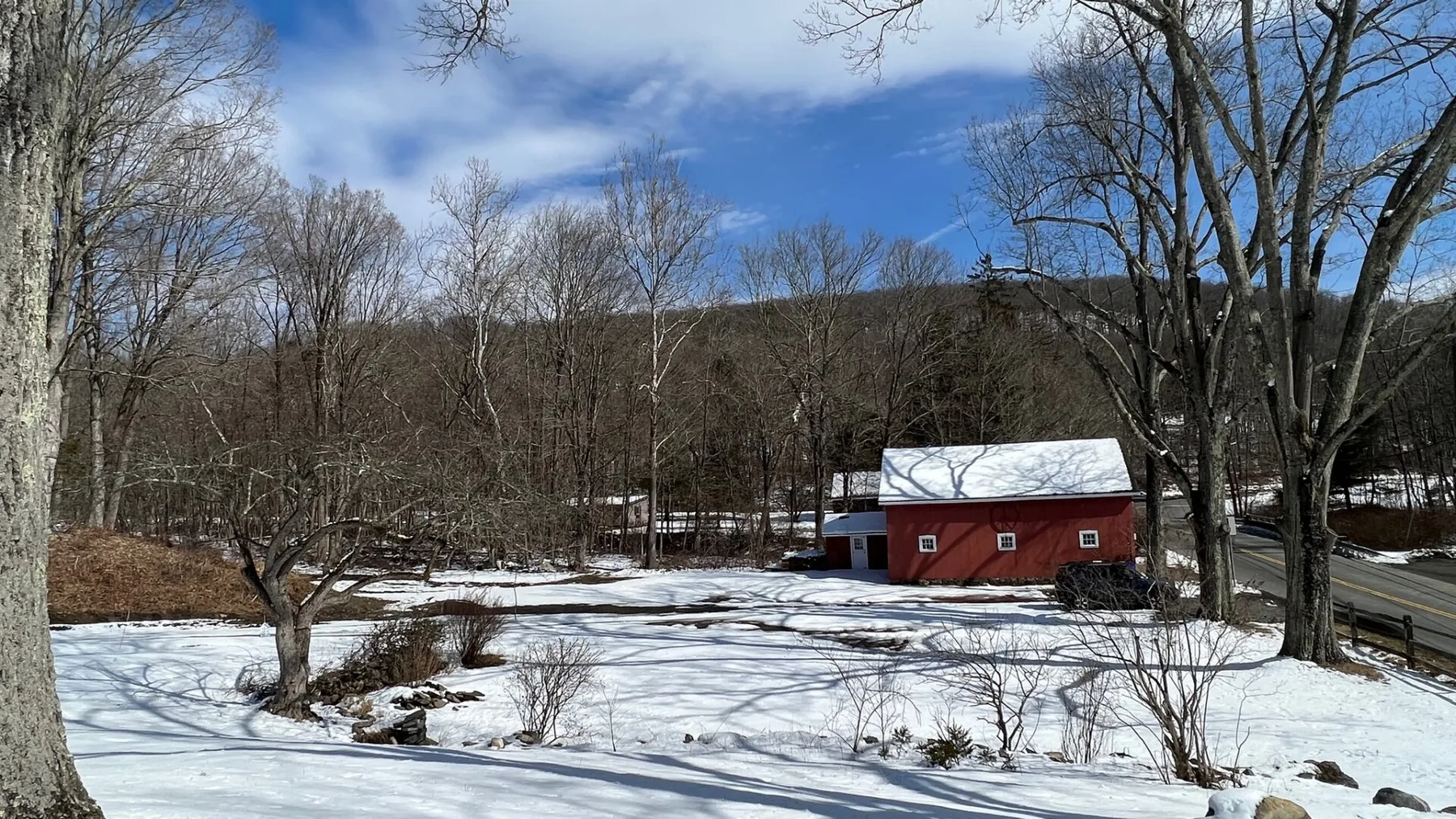 A red outbuilding sits in a snowy yard among leafless trees.