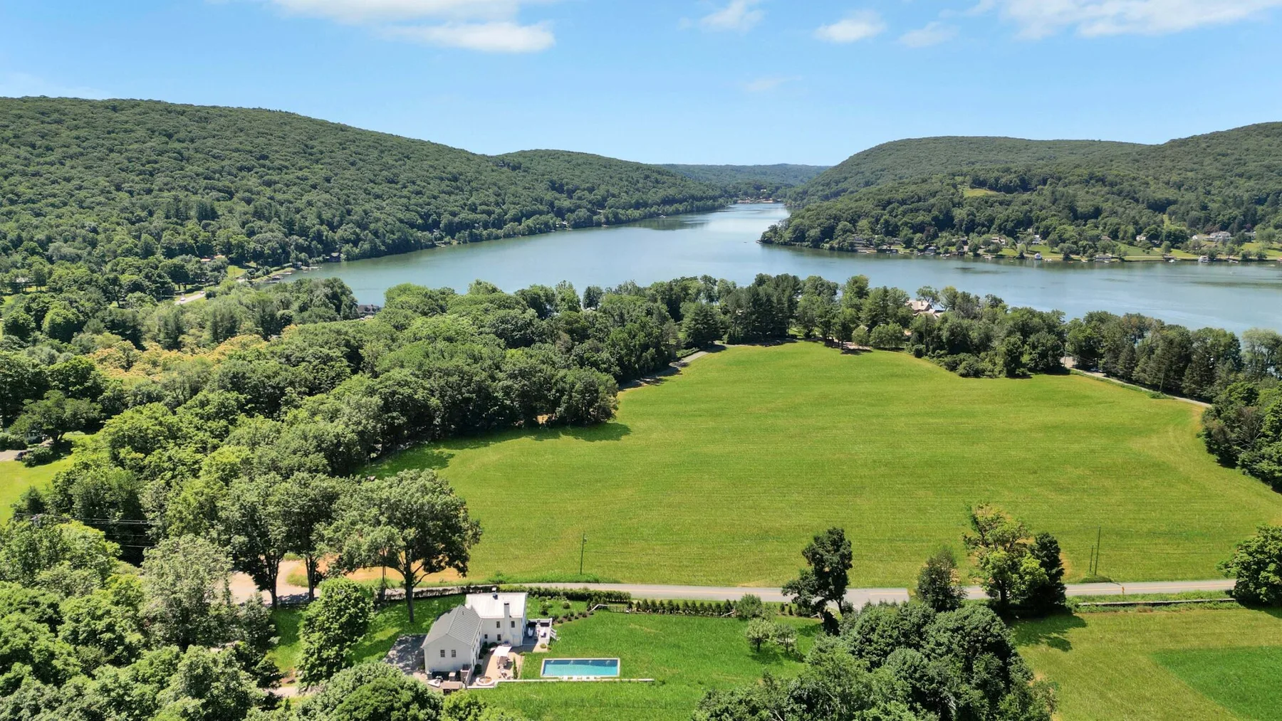 Vista aérea de un campo verde junto a un lago serpenteante y colinas boscosas.