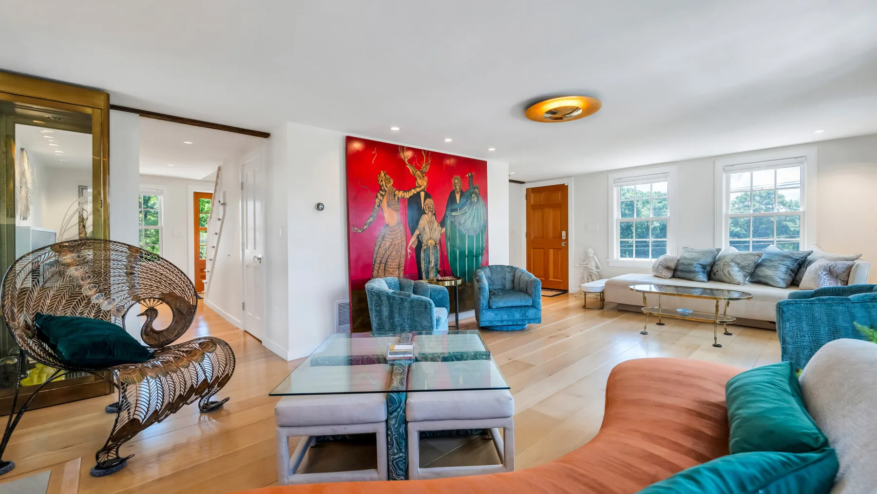 A bright living room with blue seating, a glass coffee table, and colorful wall art.