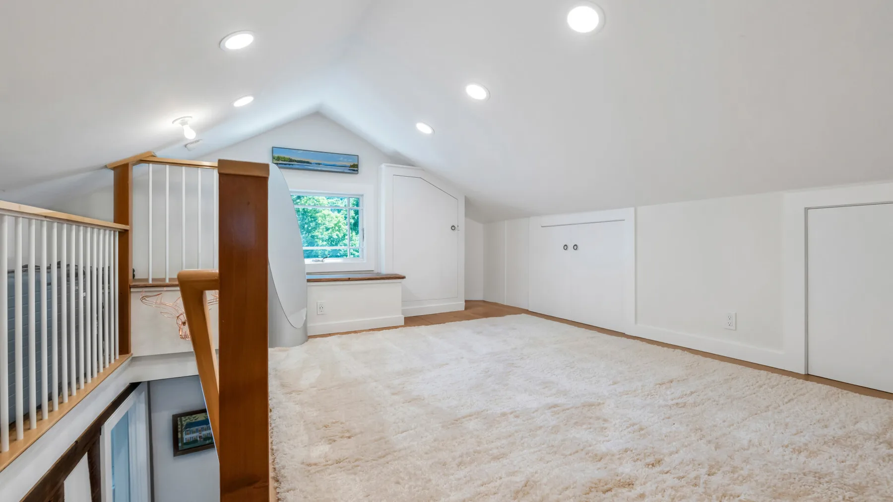 A bright attic room with a sloped ceiling, window, and carpeted floor.