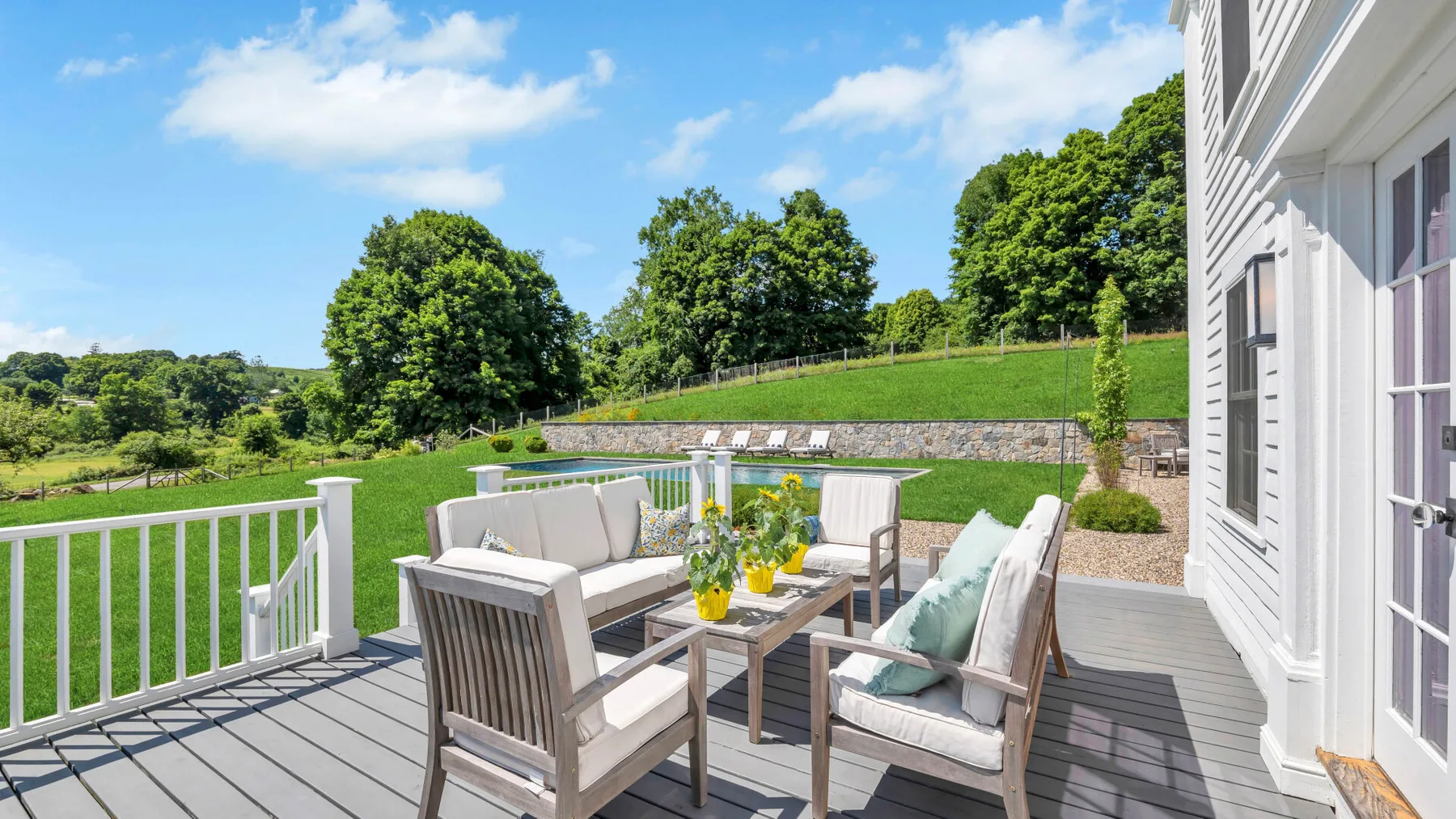 A deck with outdoor seating and a table overlooks a green landscape.