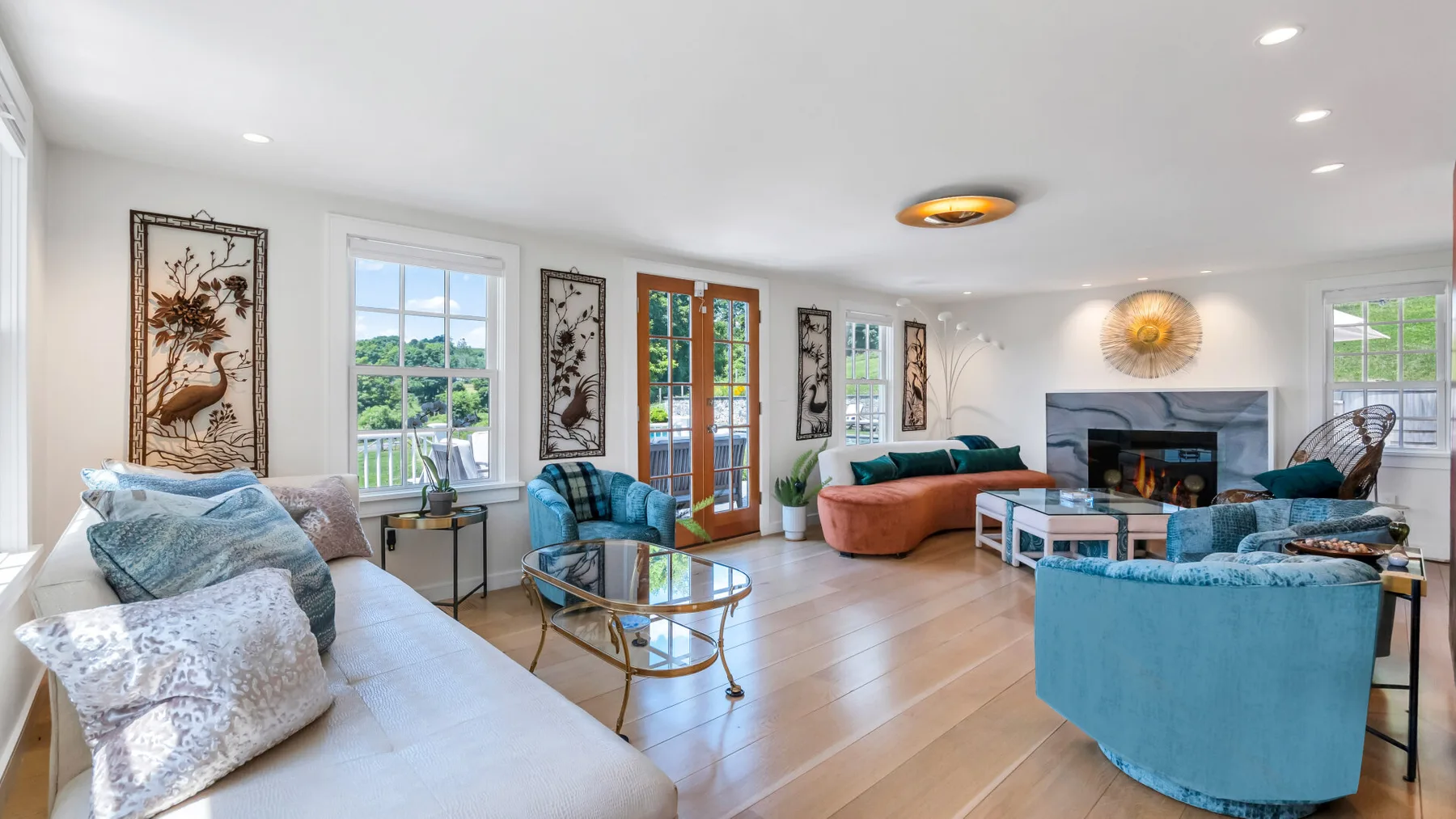 A bright living room with seating arranged around a glass coffee table and fireplace.