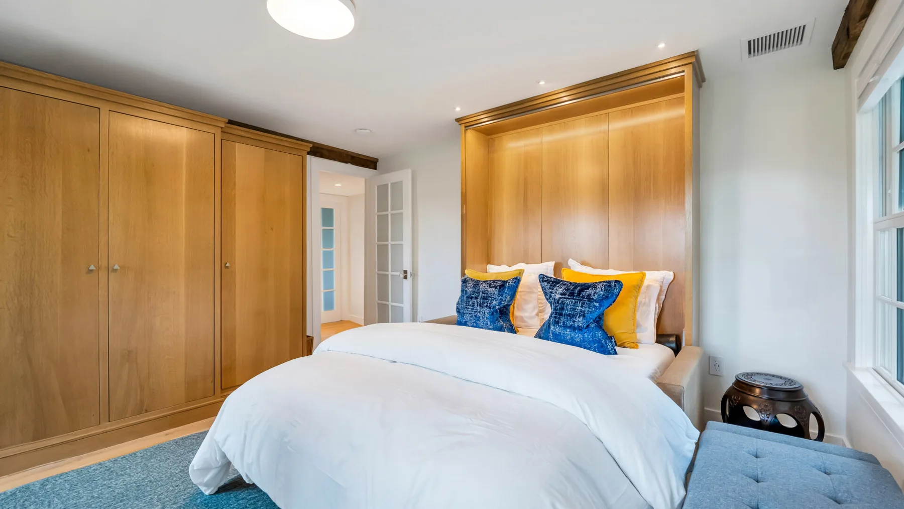 A bedroom with a bed, blue and yellow pillows, and built-in wooden cabinets.