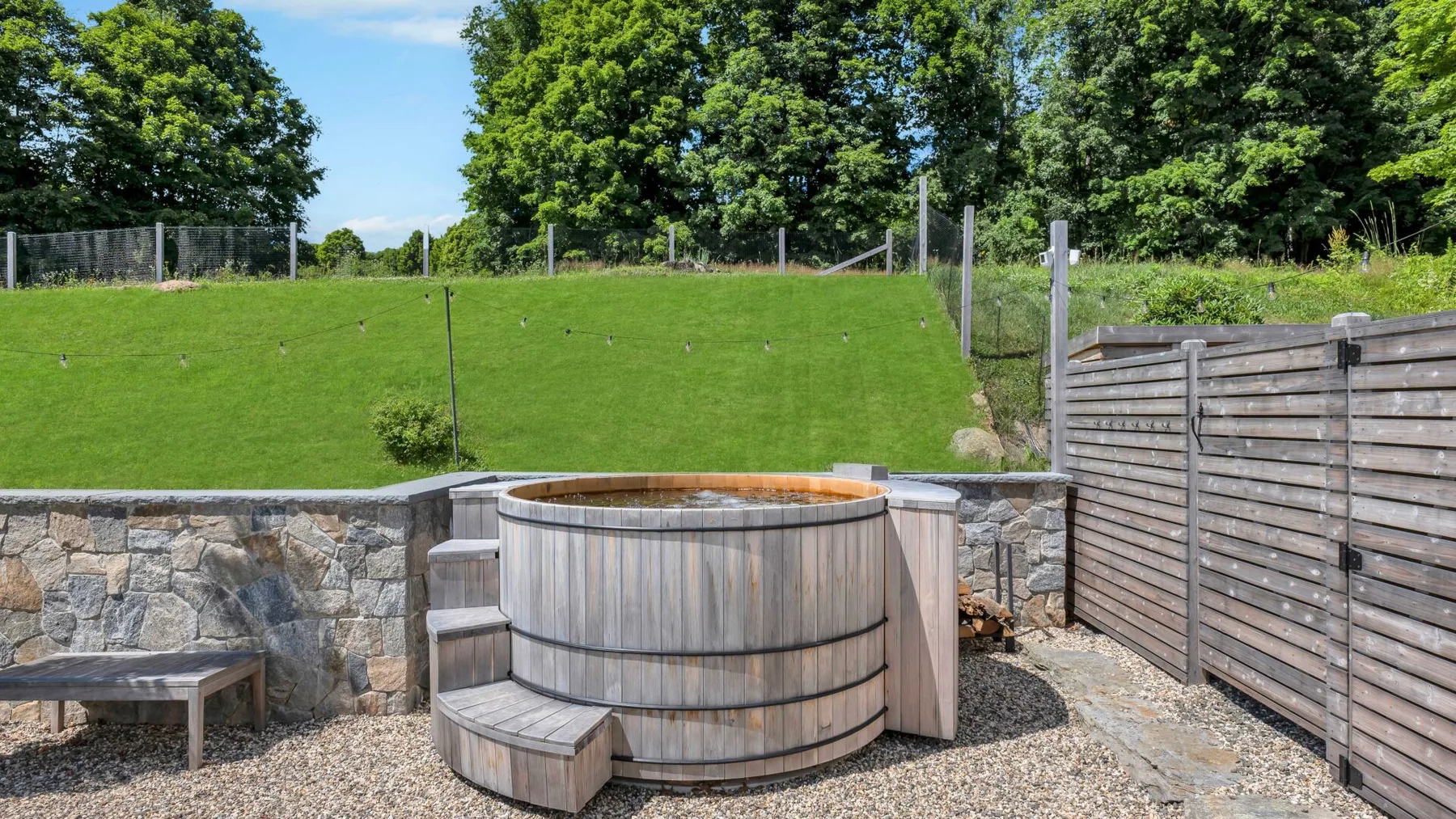 An outdoor hot tub sits beside a stone retaining wall and wooden privacy screens.