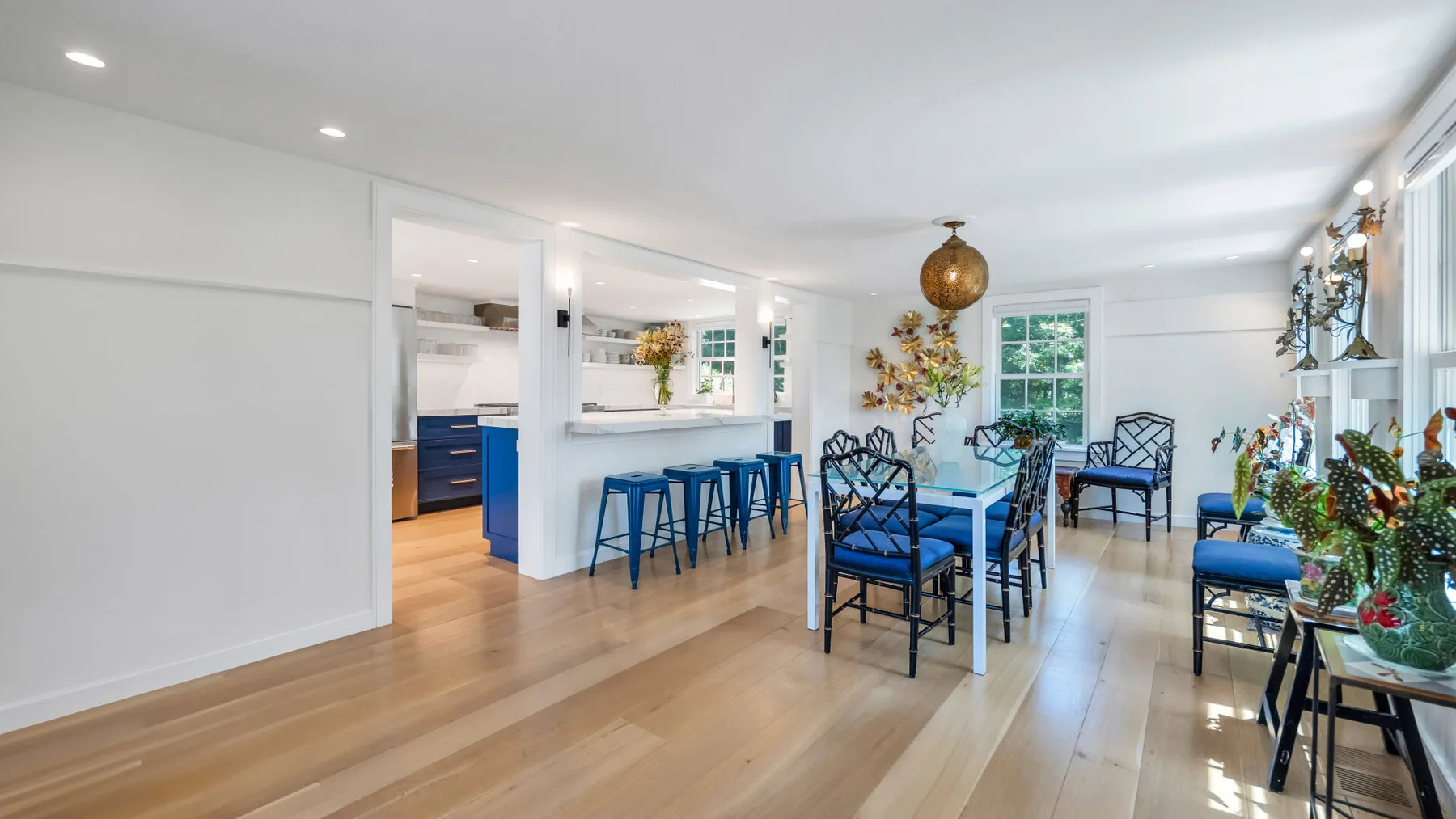A bright dining area with a long table and blue seating beside an open kitchen.