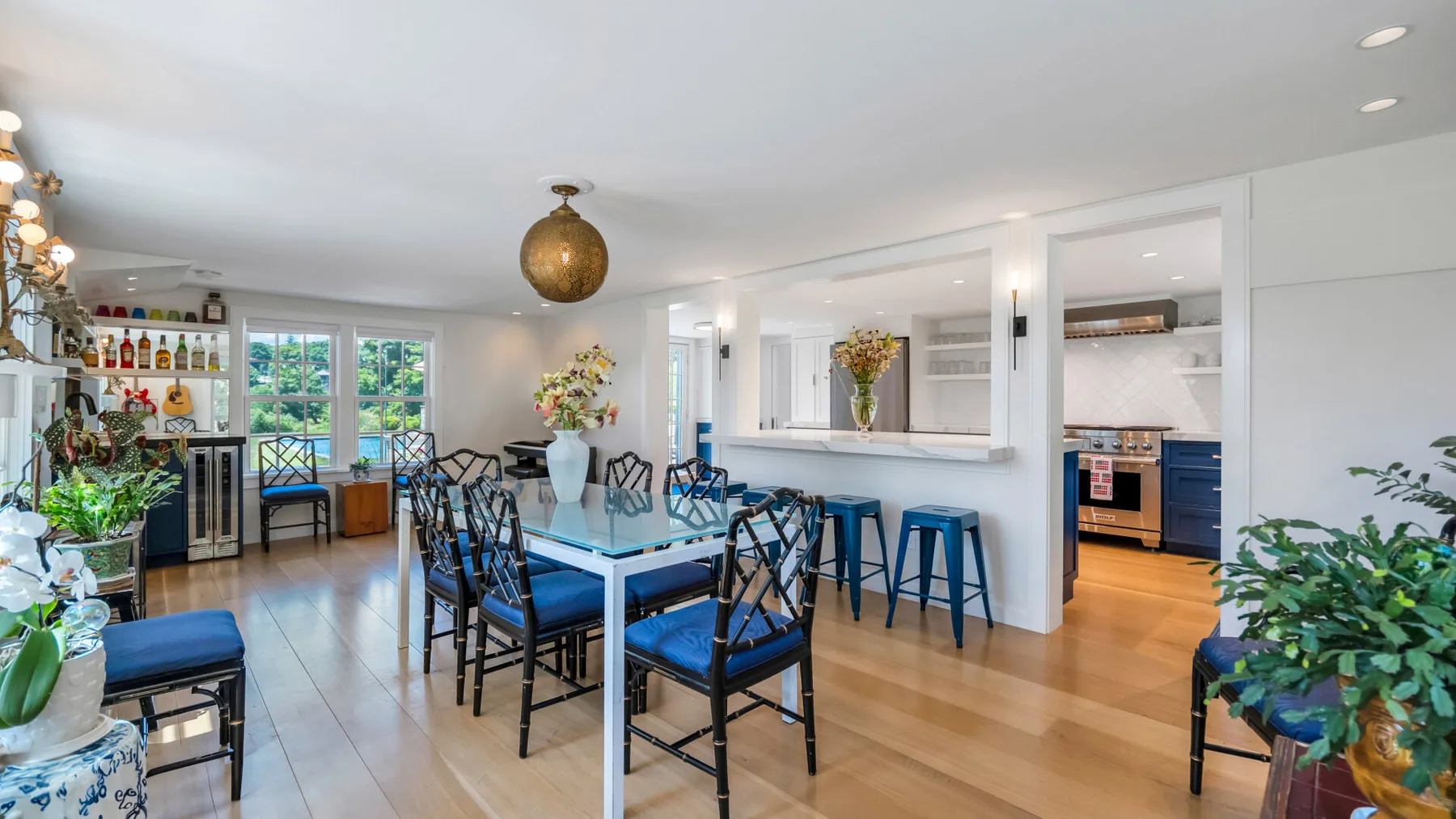 A dining area with a long table and a kitchen visible through the open pass-through.