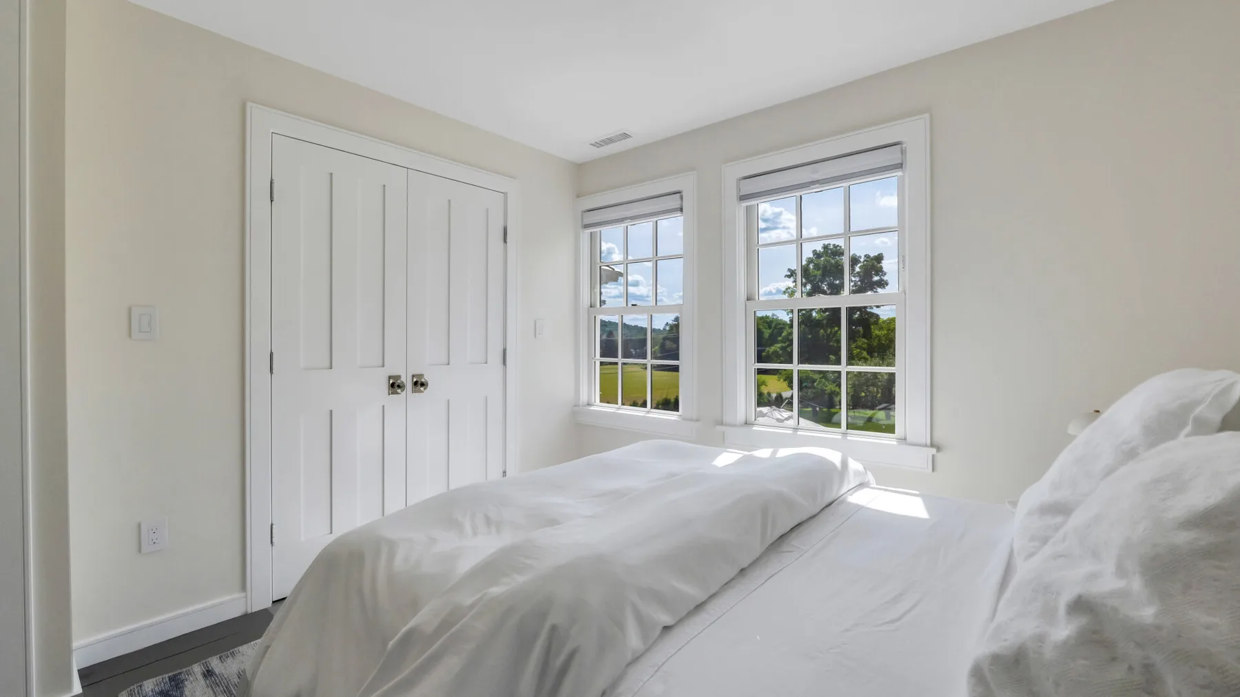 A bright bedroom with a bed beside two large windows.