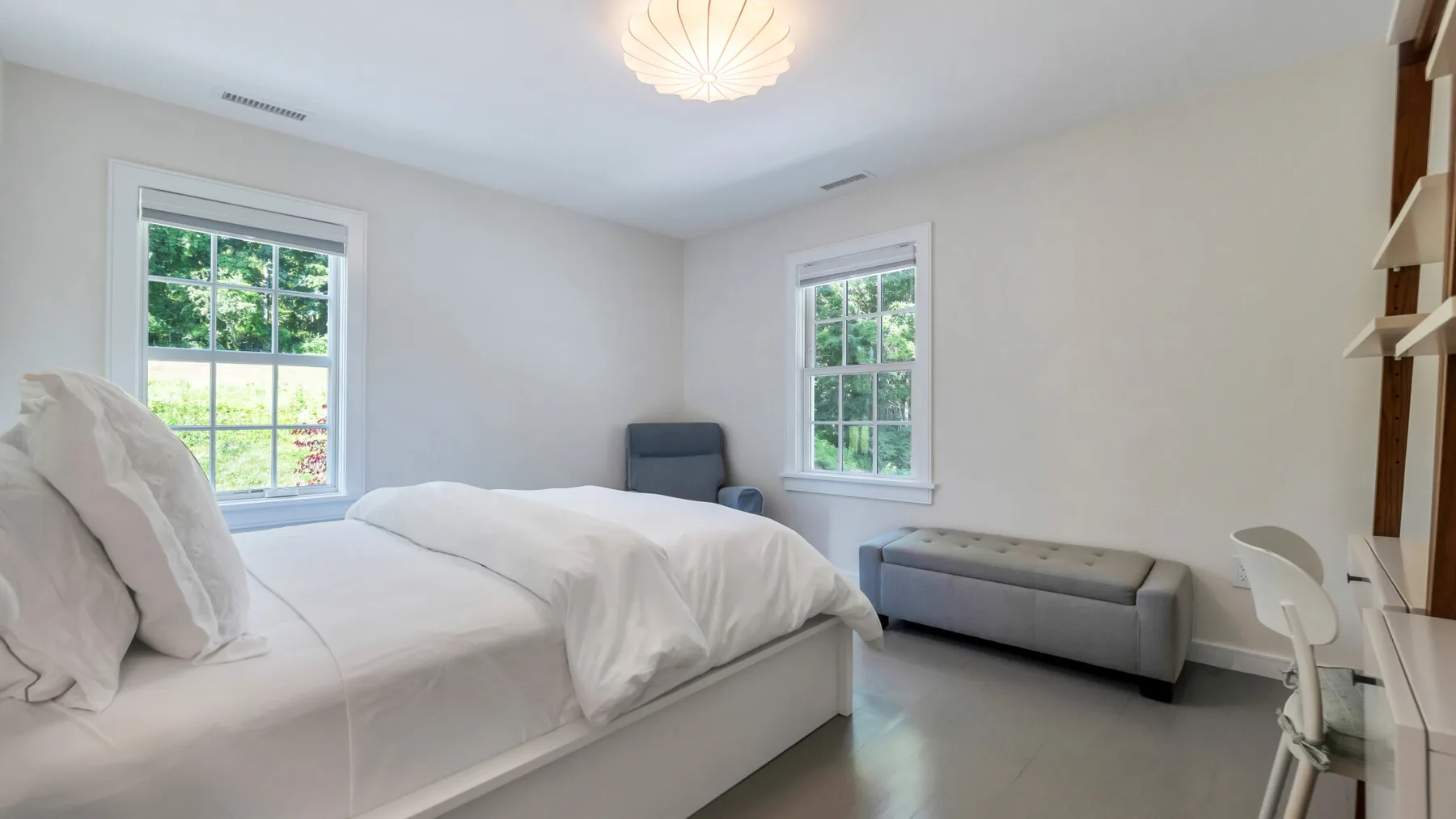 A bright bedroom with a bed, a small sofa, and two windows.