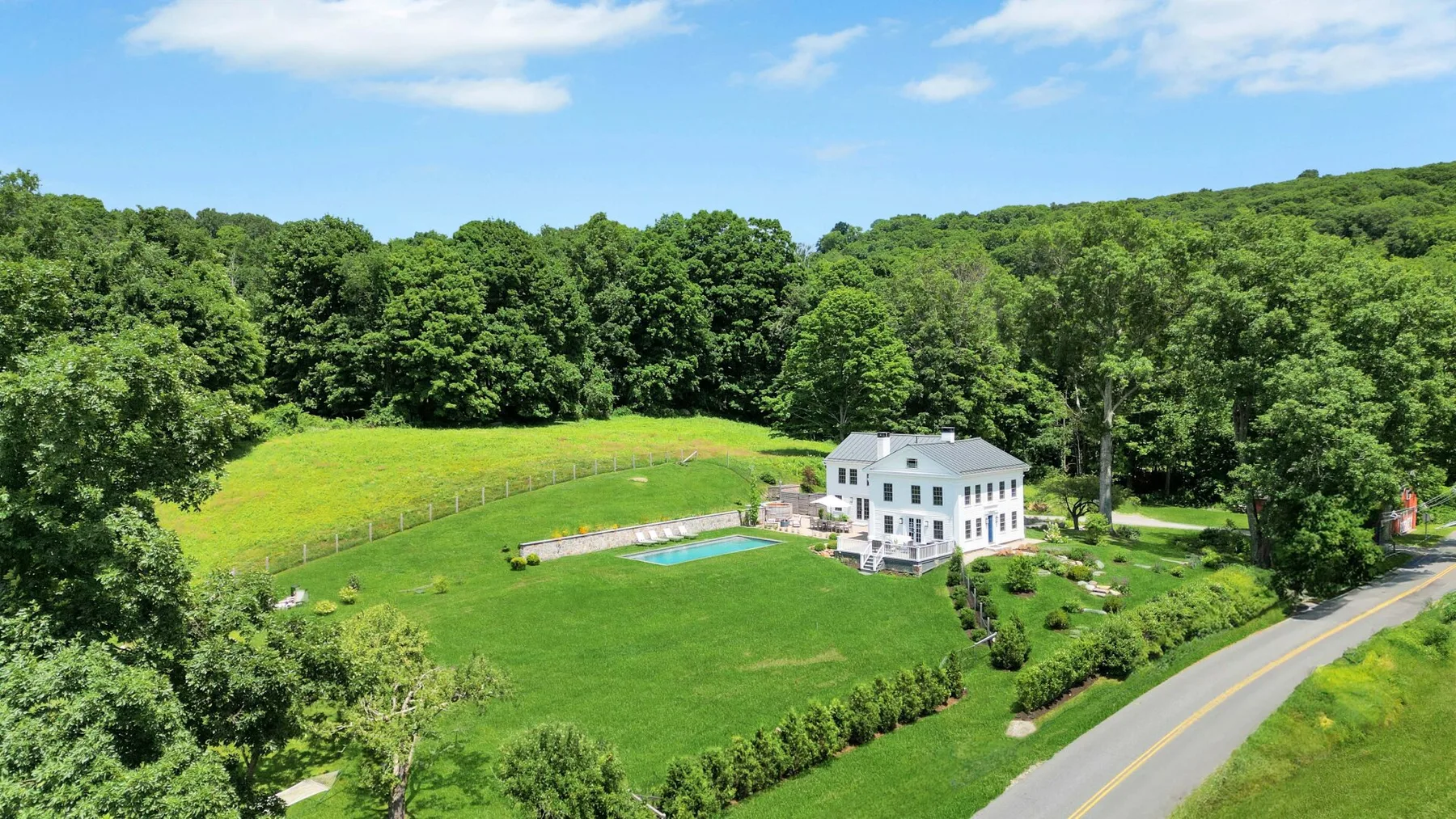 A white house overlooks a broad green lawn, with a small pool and wooded hills beyond.