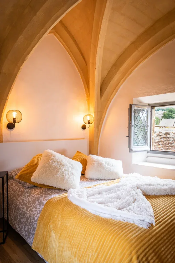 A bedroom with a bed, white bedding, and an open window beneath arched ceilings.