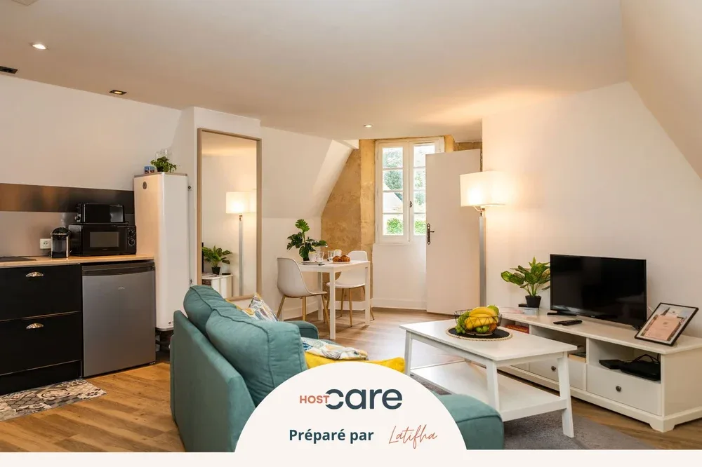 A bright living area with a teal sofa, dining table, and kitchenette.