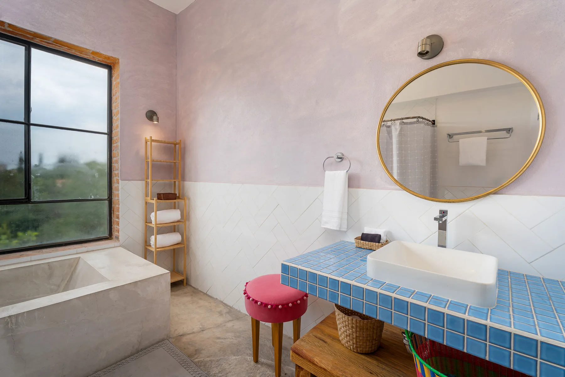 A bathroom with a blue-tiled vanity, white basin, and large round mirror.