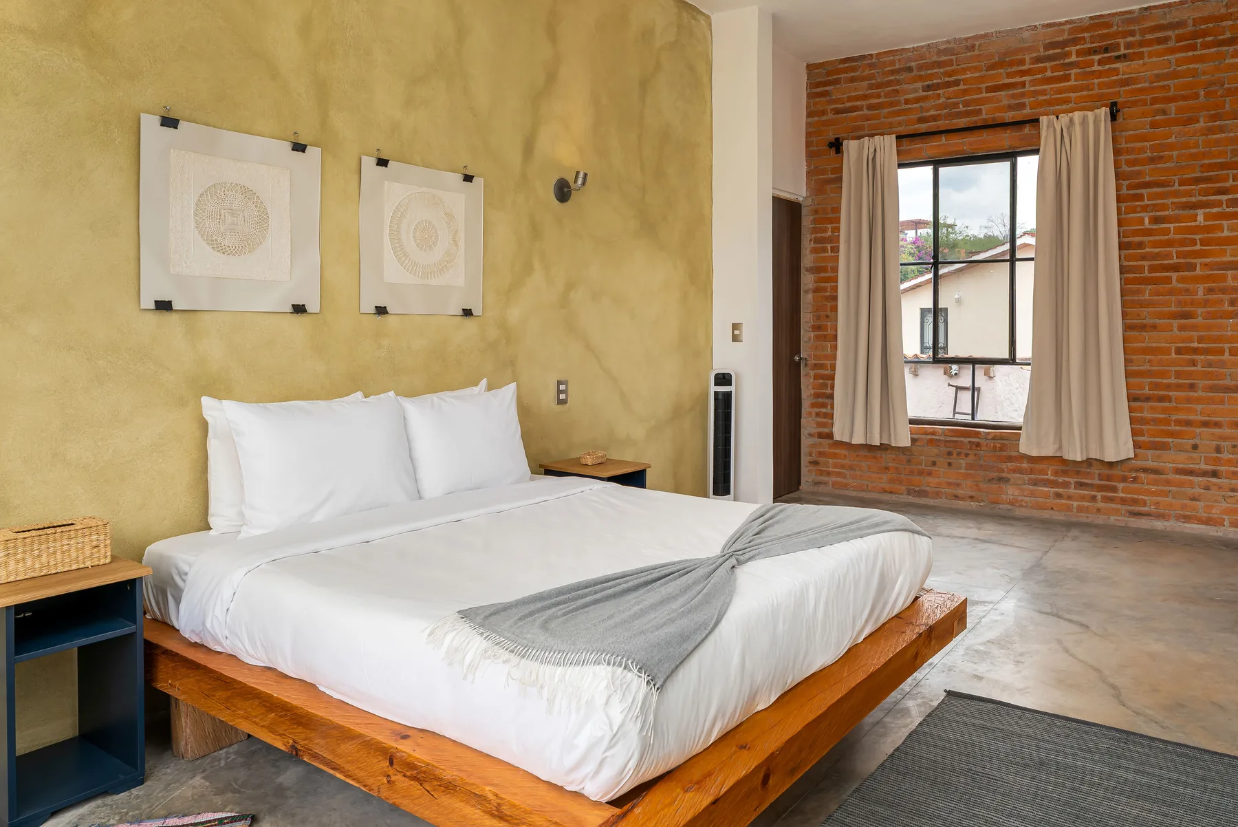 A bedroom with a neatly made bed and a window set in a brick wall.