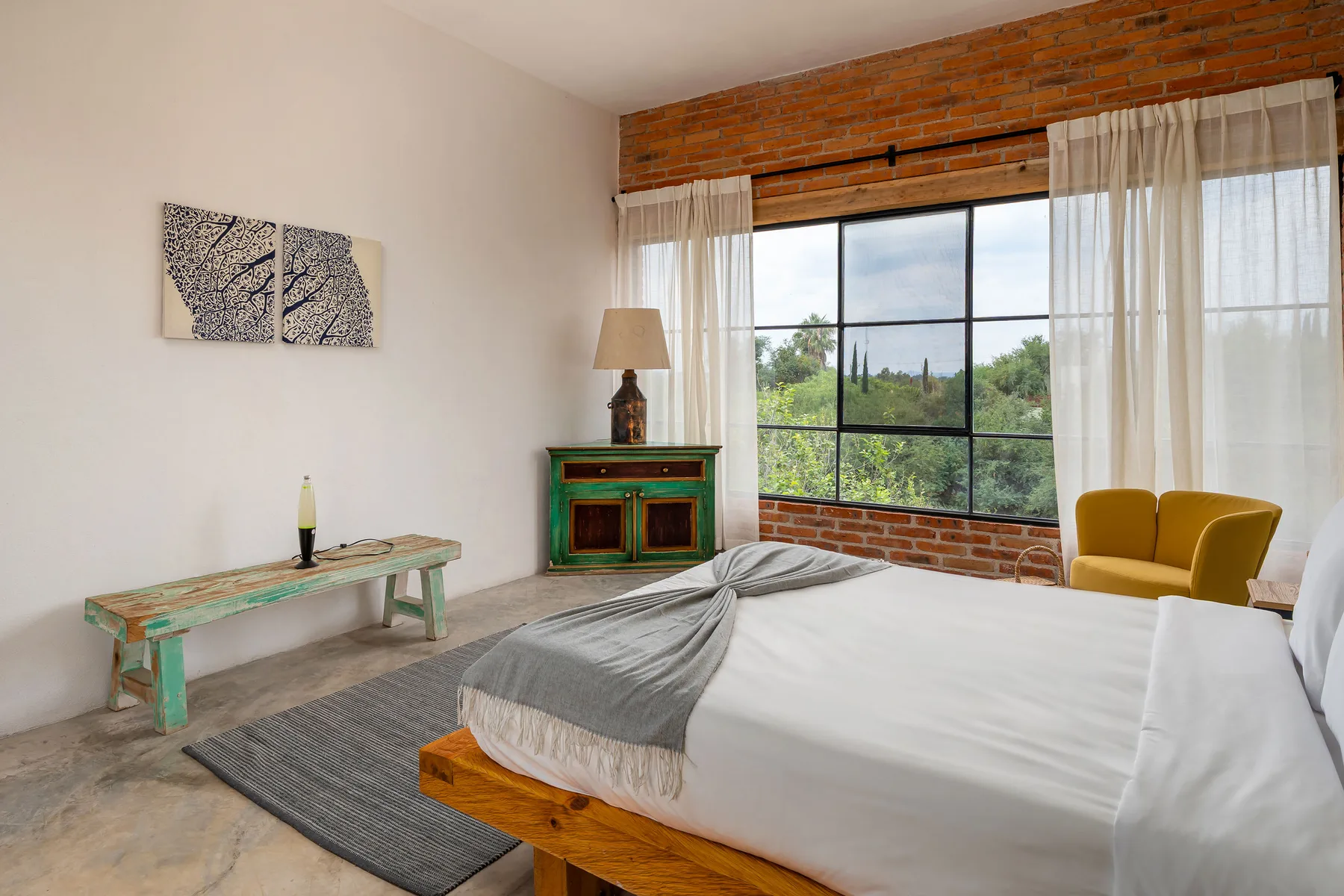 A bedroom with a bed beside a large window and yellow seating.