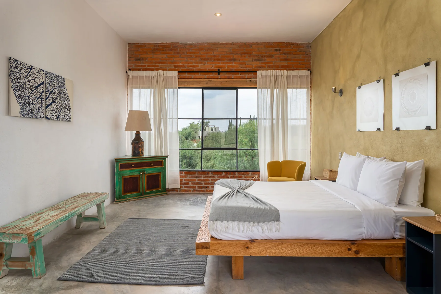 A bedroom with a large bed beside a window and a colorful wooden bench.