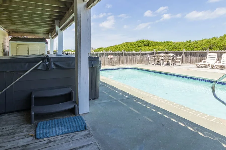 Una piscina junto a un patio sombreado con asientos.
