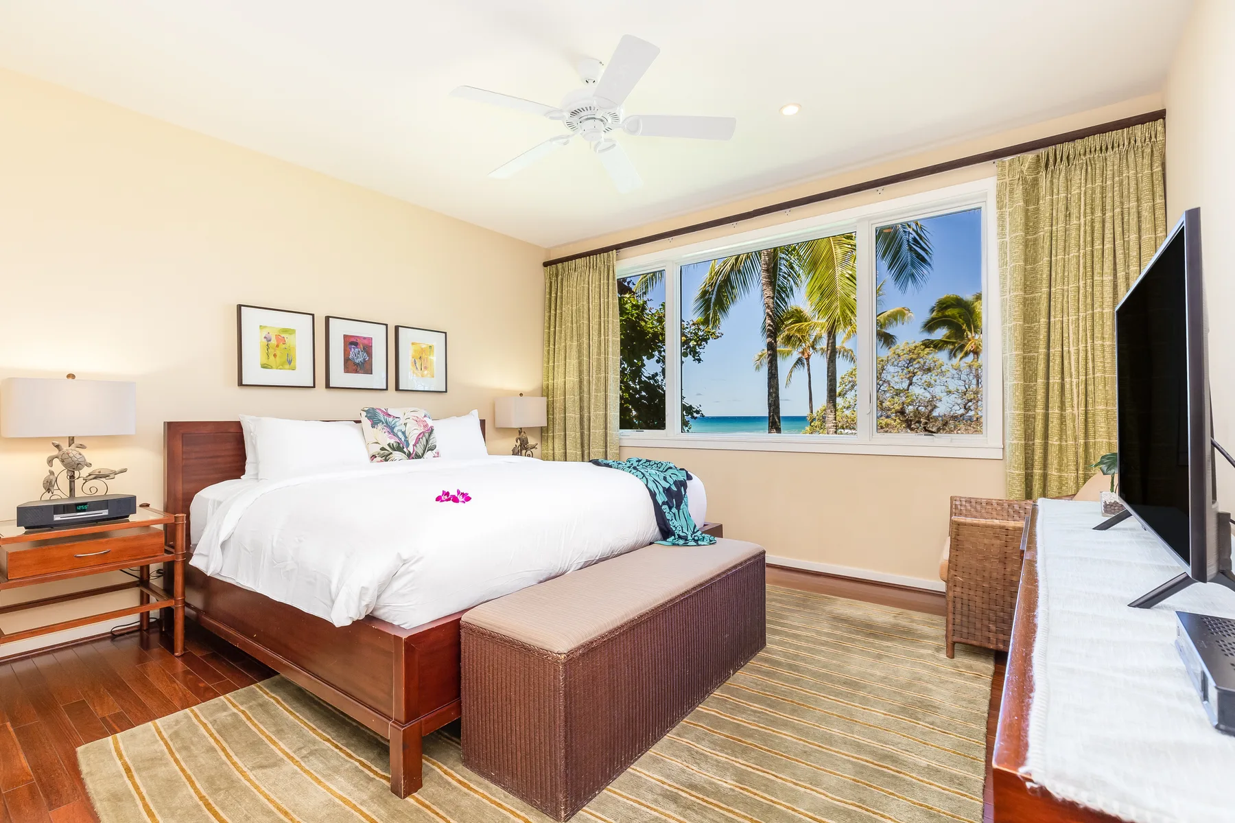 Un dormitorio con una cama grande, un televisor y ventanas con vista a palmeras.
