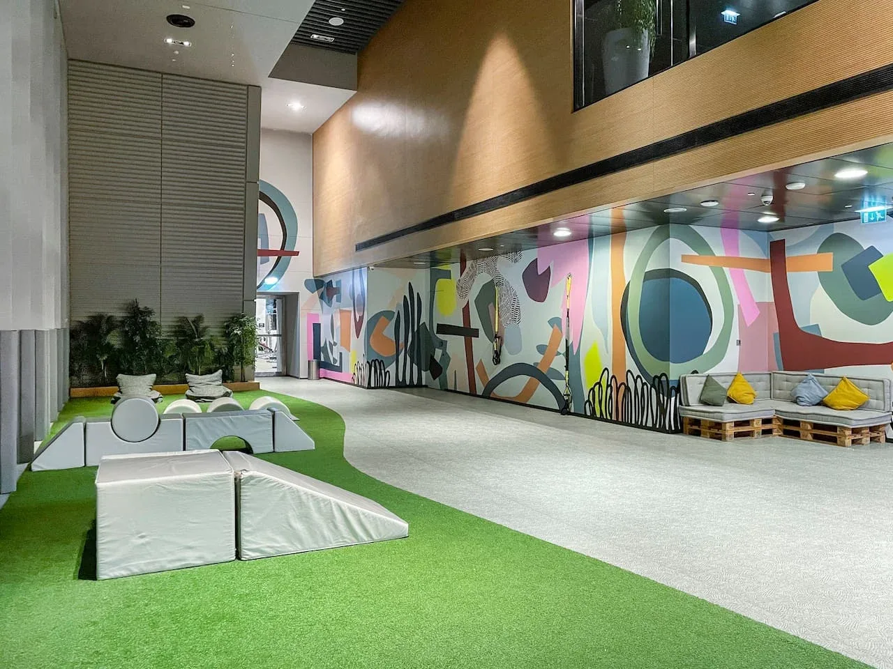 A modern lobby features colorful mural walls and seating on a green floor.