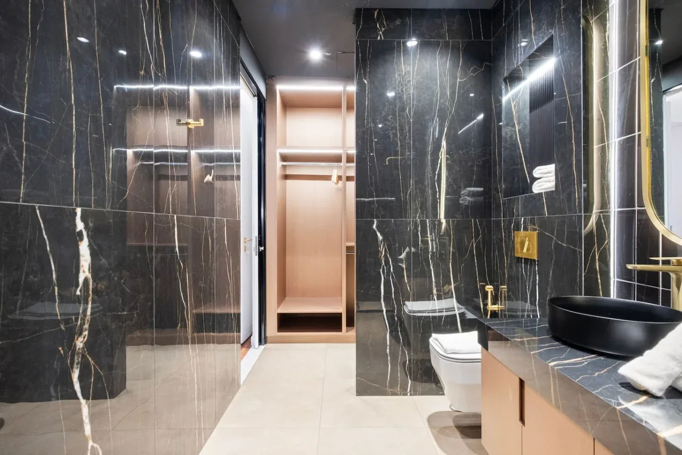 A dark marble bathroom with a glass shower, toilet, and vanity.