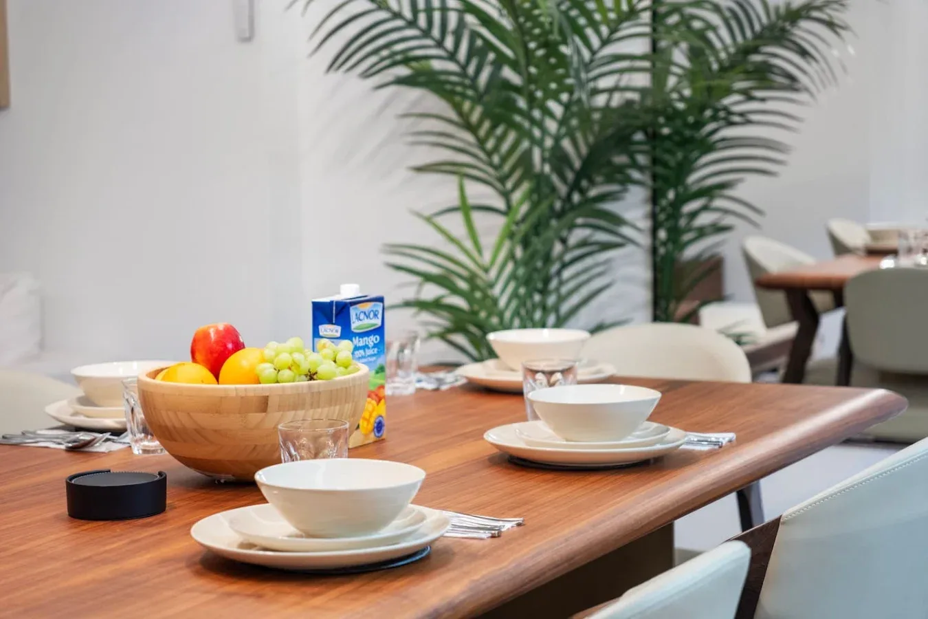 A dining table is set with bowls, plates, fruit, and a drink carton.
