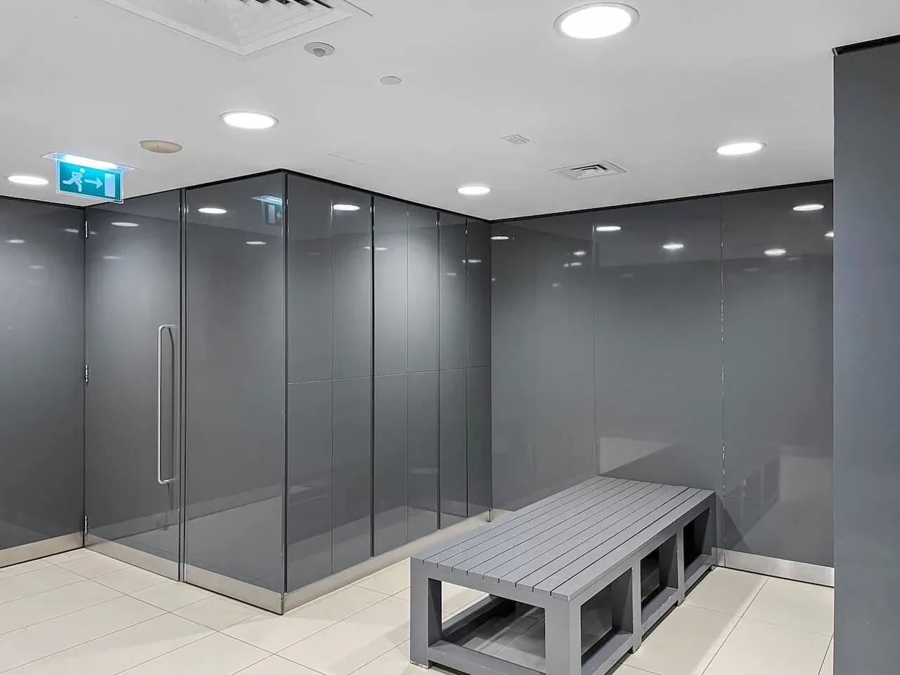 A modern changing room with a long bench and gray partition walls.