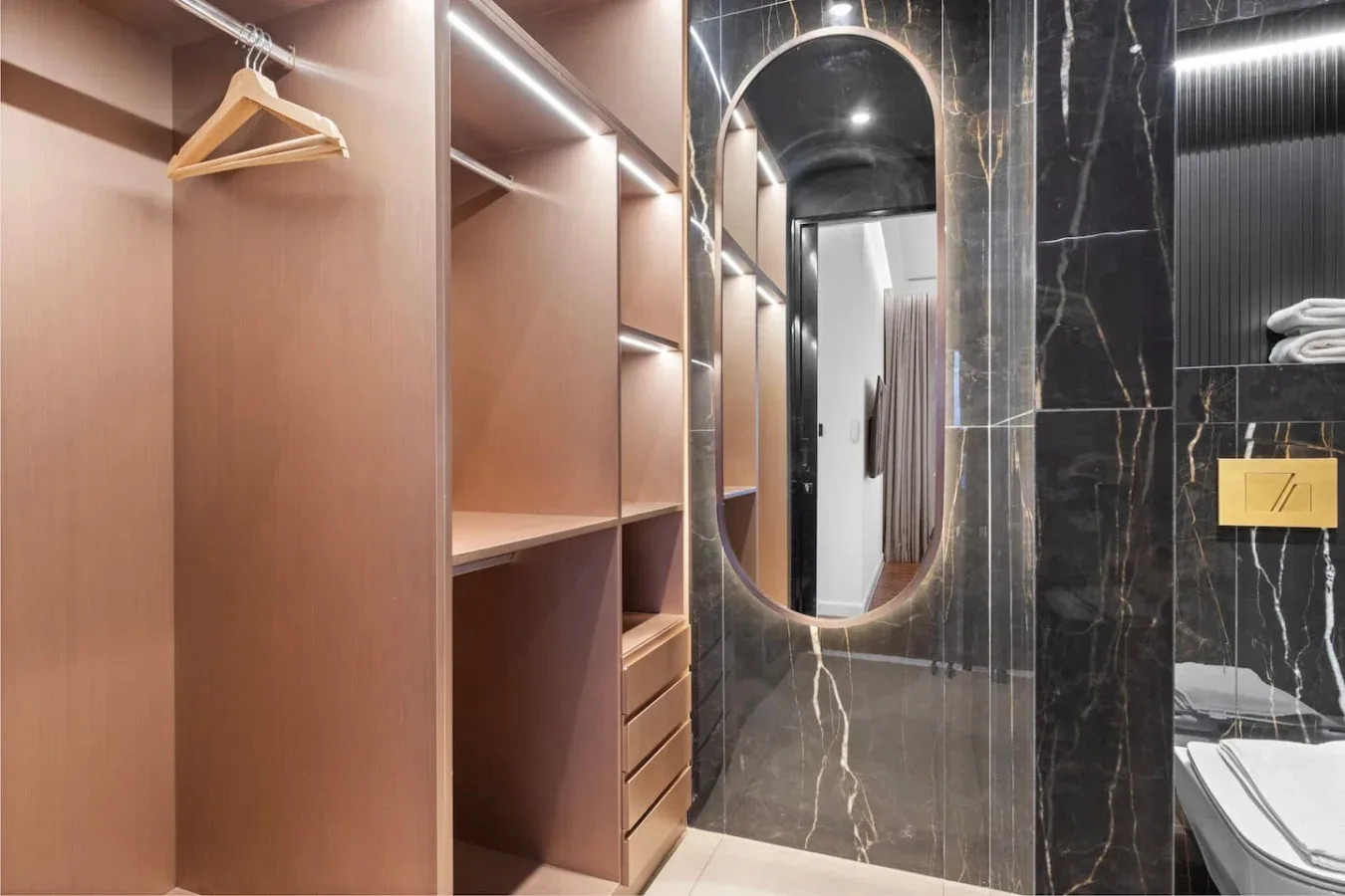 A walk-in closet with open wooden shelving beside a dark stone bathroom.